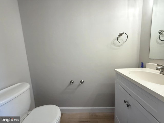 half bath with baseboards, vanity, and toilet