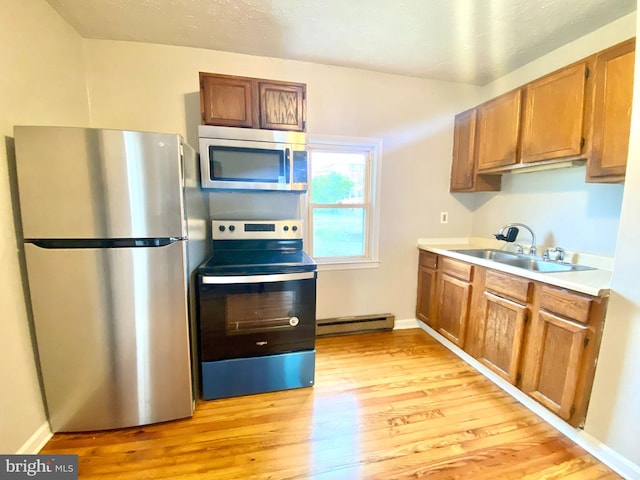 kitchen featuring light wood finished floors, stainless steel appliances, brown cabinetry, a baseboard heating unit, and a sink