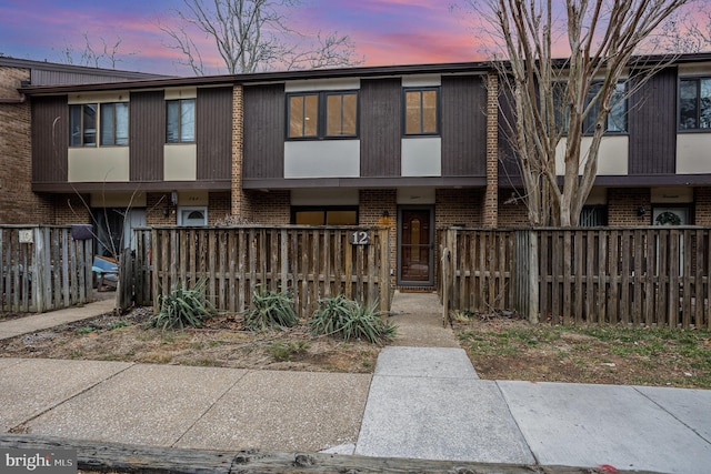 townhome / multi-family property featuring covered porch, a fenced front yard, and brick siding