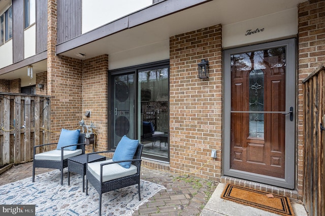 doorway to property featuring brick siding, a patio area, and fence