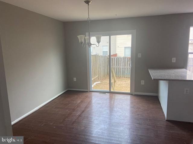 unfurnished dining area featuring dark wood-type flooring, a notable chandelier, and baseboards