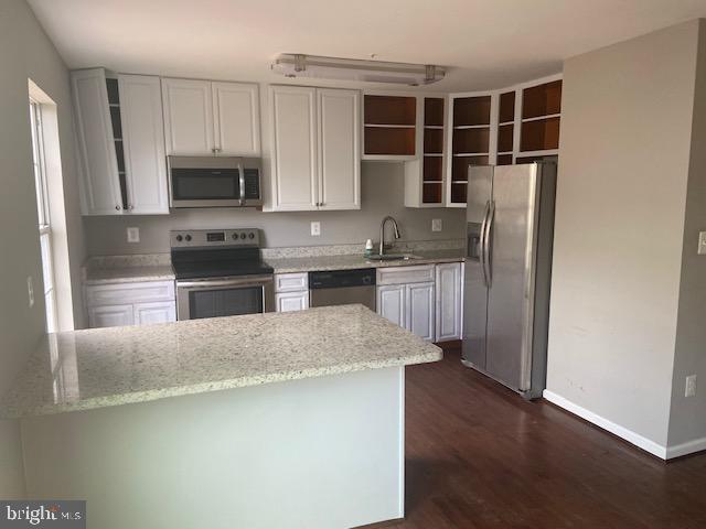 kitchen with dark wood-style floors, light stone countertops, baseboards, a sink, and stainless steel appliances