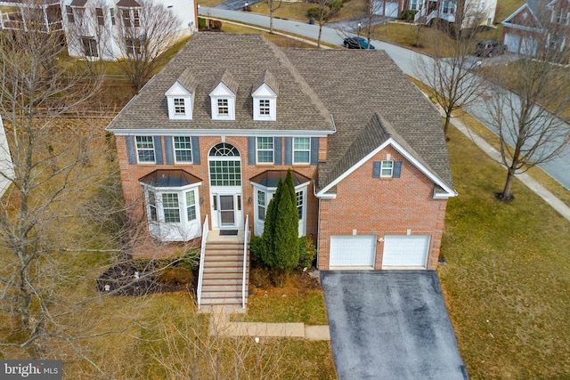 view of front of house with driveway, roof with shingles, stairs, a garage, and brick siding