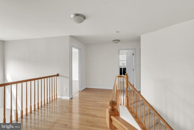 hall featuring baseboards, an upstairs landing, and light wood-style flooring