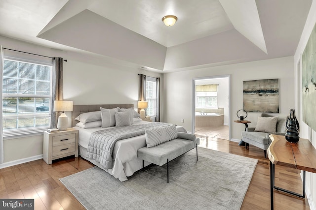 bedroom featuring ensuite bathroom, baseboards, a raised ceiling, and light wood-style floors