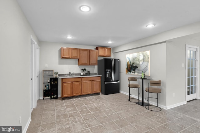 kitchen featuring a sink, black fridge with ice dispenser, recessed lighting, light countertops, and baseboards