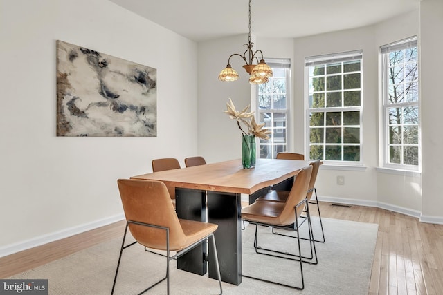 dining space with visible vents, baseboards, a notable chandelier, and light wood-style flooring