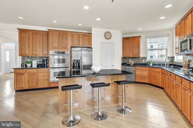 kitchen featuring light wood finished floors, stainless steel appliances, decorative backsplash, a kitchen bar, and a center island