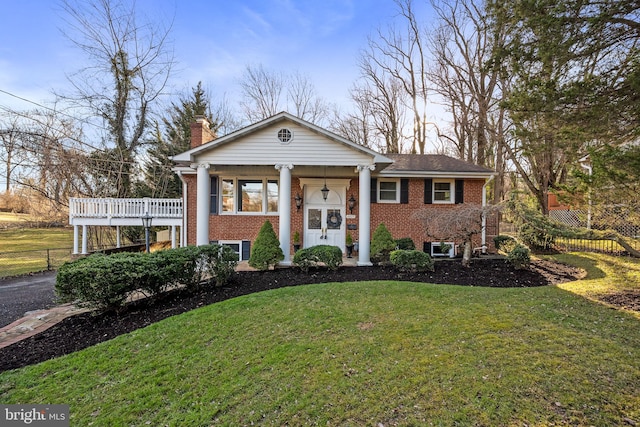 greek revival inspired property featuring a front yard, a chimney, fence, and brick siding