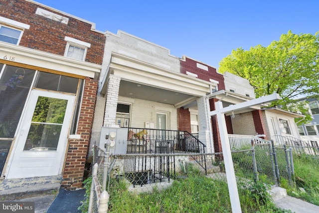 view of front of home with a porch, brick siding, and fence