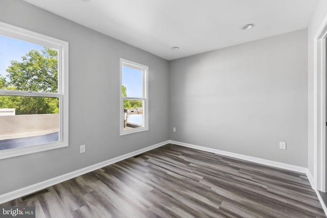 unfurnished room featuring dark wood-style flooring, visible vents, and baseboards