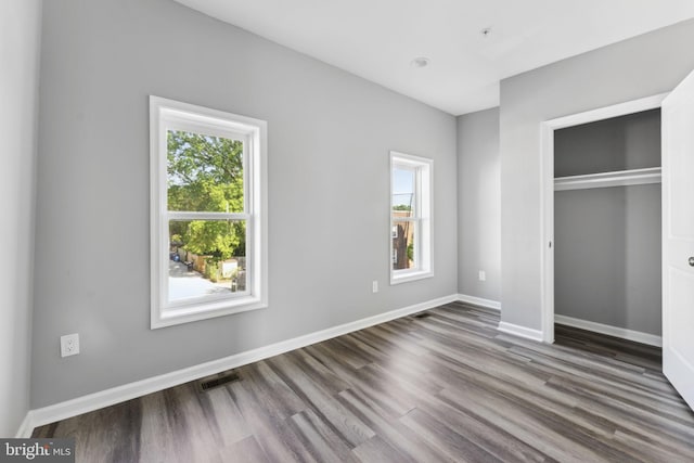 unfurnished bedroom featuring multiple windows, wood finished floors, visible vents, and baseboards