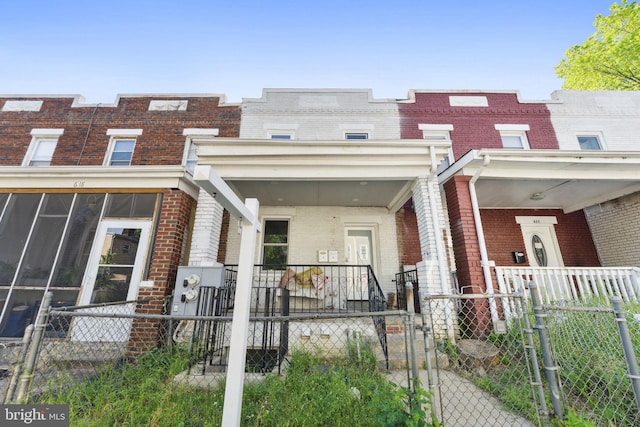 view of front facade featuring covered porch, brick siding, a fenced front yard, and a gate