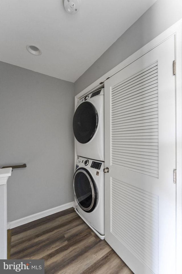 clothes washing area featuring laundry area, baseboards, dark wood finished floors, and stacked washing maching and dryer