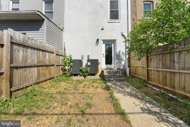 property entrance with stucco siding, fence, and central air condition unit