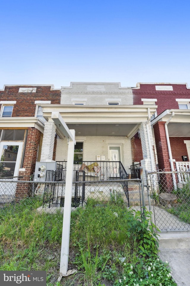 view of front facade featuring a porch, a fenced front yard, a gate, and brick siding