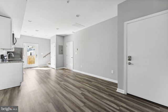 unfurnished living room with electric panel, stairs, baseboards, and dark wood-style flooring