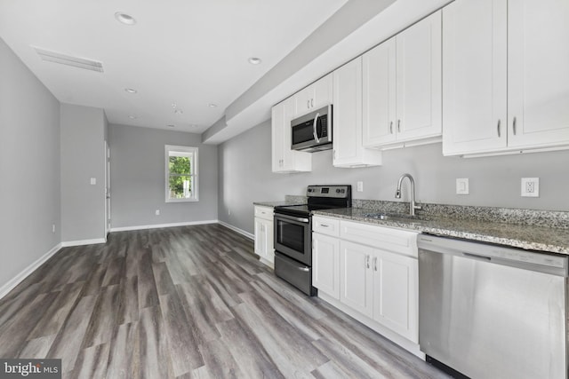 kitchen with light stone counters, appliances with stainless steel finishes, a sink, wood finished floors, and baseboards