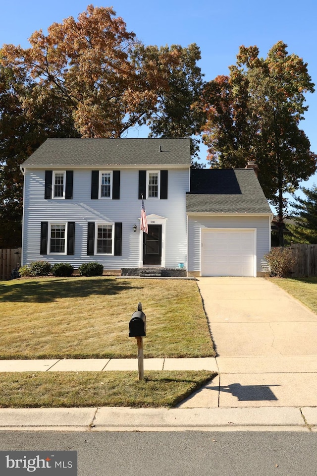 colonial-style house with an attached garage, concrete driveway, a front yard, and fence