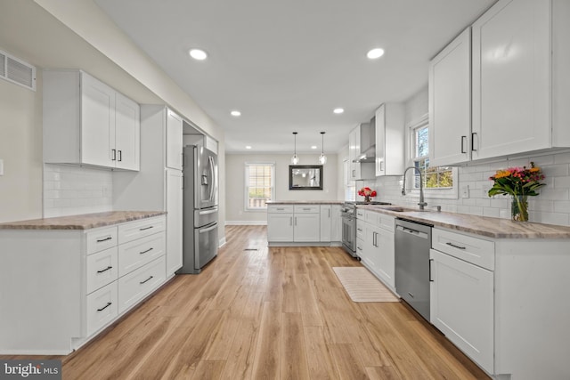 kitchen with light stone countertops, a peninsula, light wood-style flooring, a sink, and appliances with stainless steel finishes