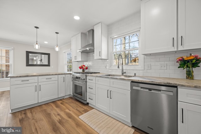 kitchen featuring a peninsula, wood finished floors, stainless steel appliances, wall chimney exhaust hood, and a sink