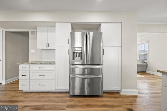 kitchen with backsplash, stainless steel fridge, light wood-style floors, white cabinets, and baseboards