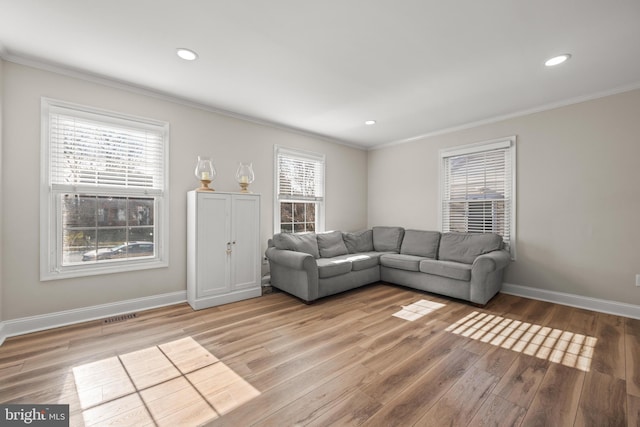 living area featuring a healthy amount of sunlight, baseboards, light wood-style floors, and ornamental molding