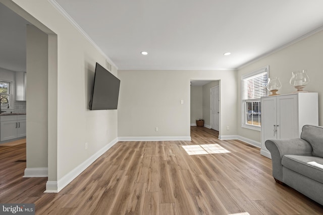 living area featuring a healthy amount of sunlight, light wood-type flooring, and ornamental molding