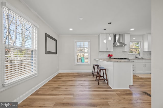 kitchen with tasteful backsplash, wall chimney range hood, a breakfast bar area, light wood-style floors, and white cabinetry