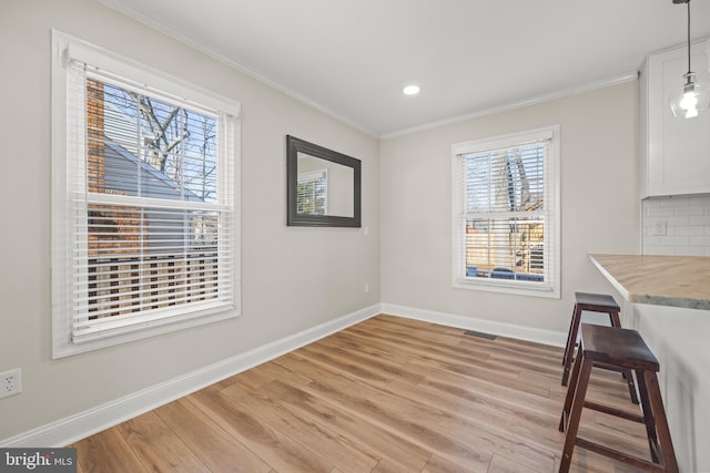 unfurnished dining area with visible vents, light wood-style floors, baseboards, and ornamental molding