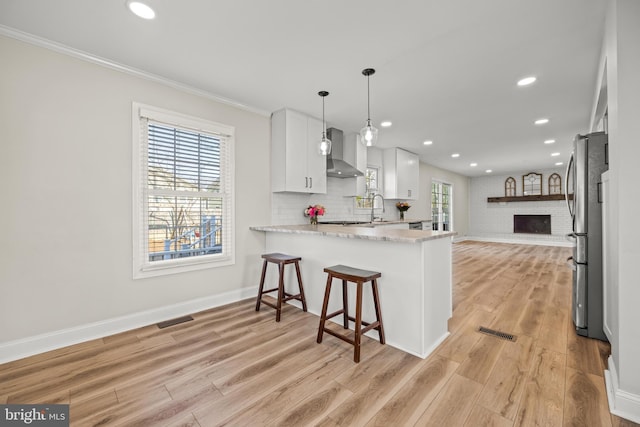 kitchen featuring open floor plan, wall chimney range hood, visible vents, and freestanding refrigerator