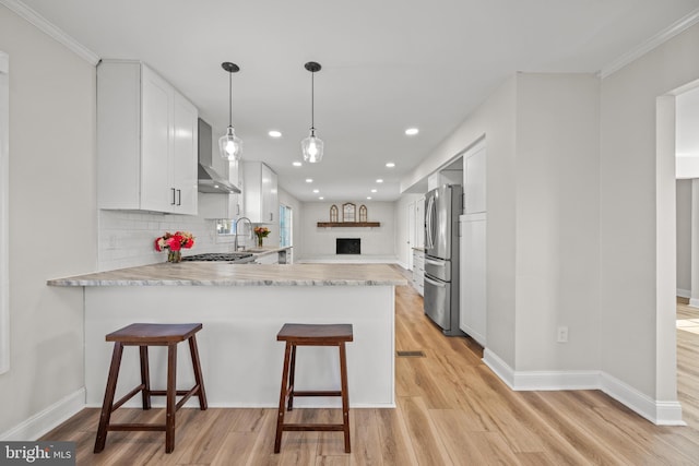 kitchen with wall chimney exhaust hood, a peninsula, light countertops, and light wood-type flooring