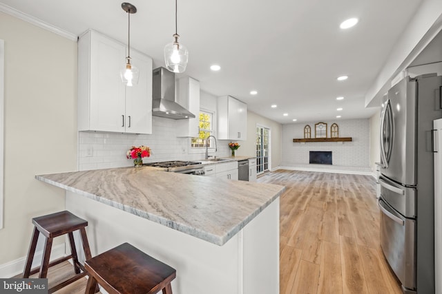 kitchen featuring light wood-style flooring, a sink, open floor plan, stainless steel appliances, and wall chimney exhaust hood