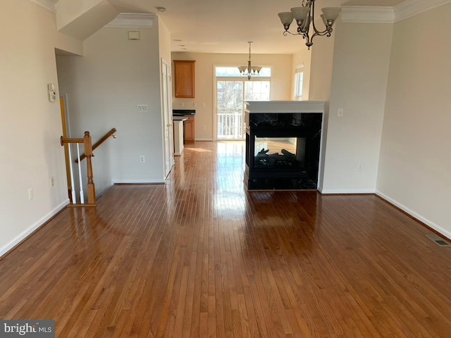 unfurnished living room featuring dark wood-style flooring, a multi sided fireplace, visible vents, baseboards, and an inviting chandelier