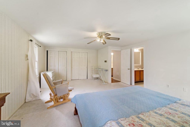 bedroom featuring multiple closets, a ceiling fan, light carpet, a sink, and ensuite bath