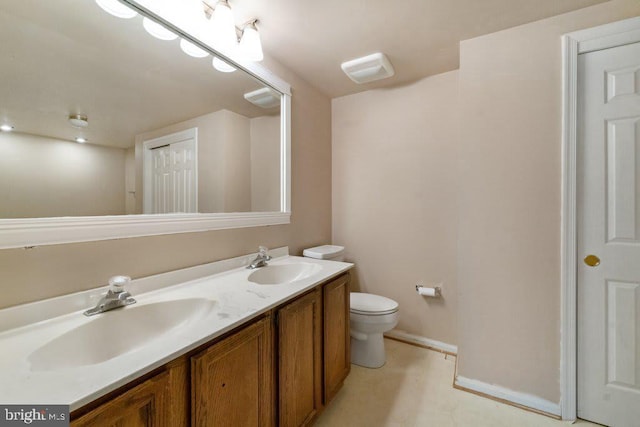 bathroom with baseboards, a sink, toilet, and double vanity