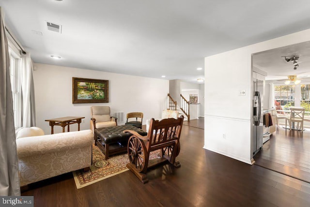 living room featuring dark wood-style flooring, visible vents, ceiling fan, and stairway