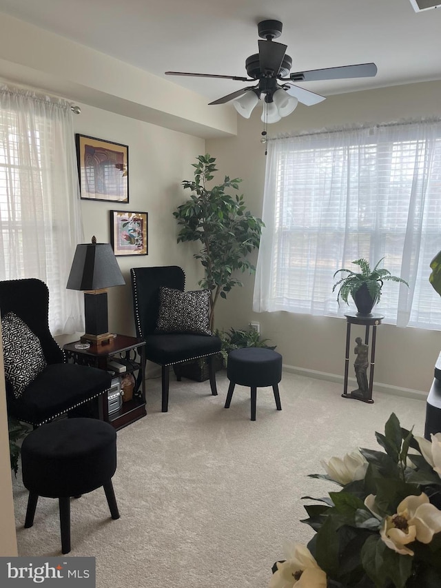 living area featuring ceiling fan, baseboards, and light carpet