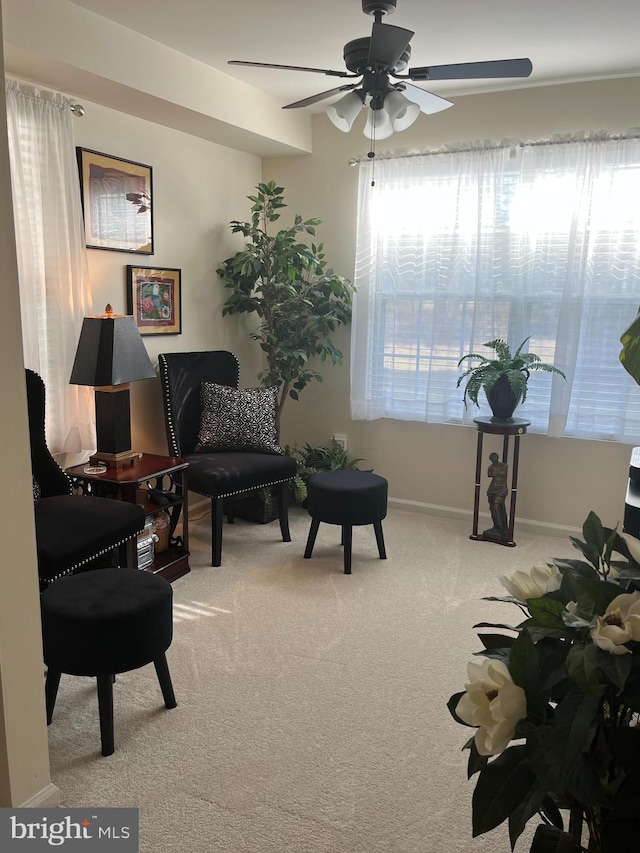 living area featuring light carpet, a ceiling fan, and baseboards