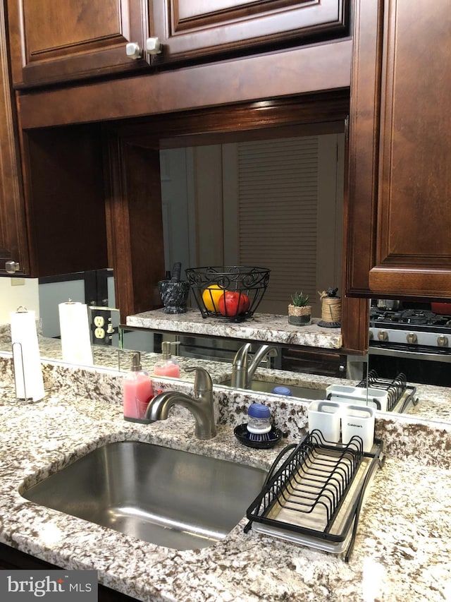 kitchen with dark brown cabinetry, light stone countertops, and a sink