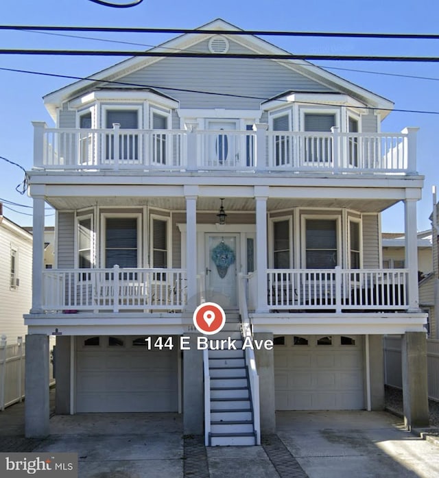 coastal inspired home featuring covered porch, driveway, stairway, and an attached garage