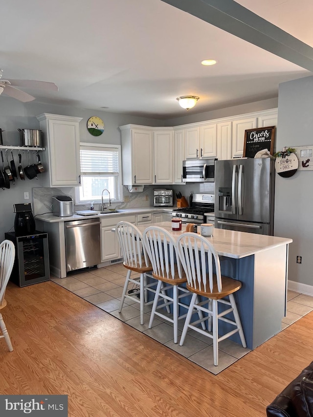 kitchen with beverage cooler, appliances with stainless steel finishes, white cabinets, and a sink