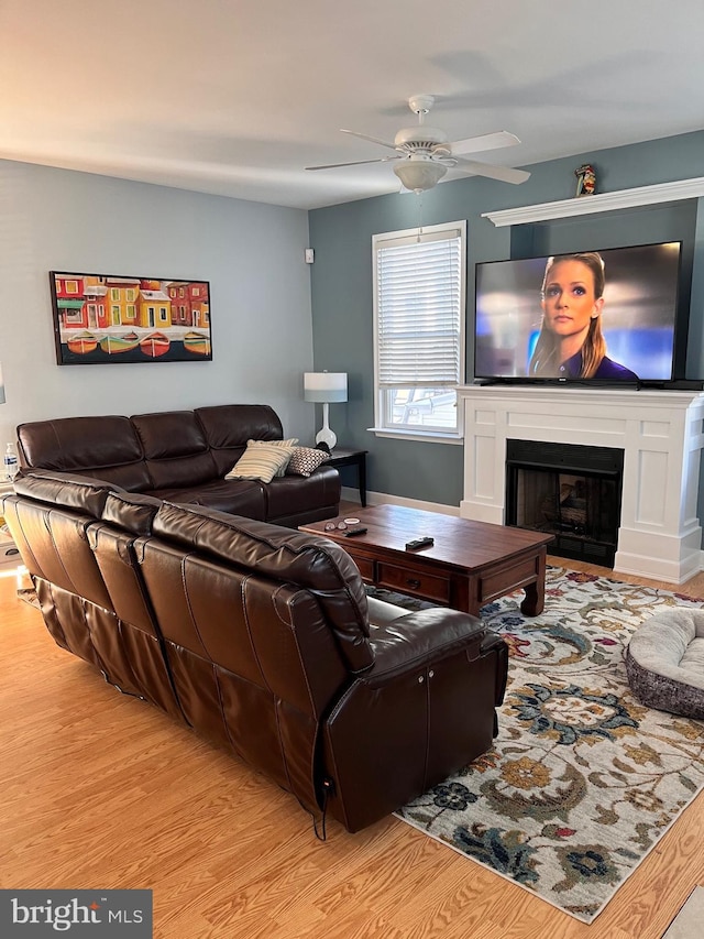 living area featuring light wood-type flooring, ceiling fan, and a fireplace