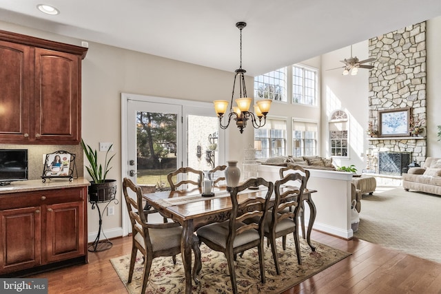 dining room featuring ceiling fan with notable chandelier, a stone fireplace, and wood finished floors