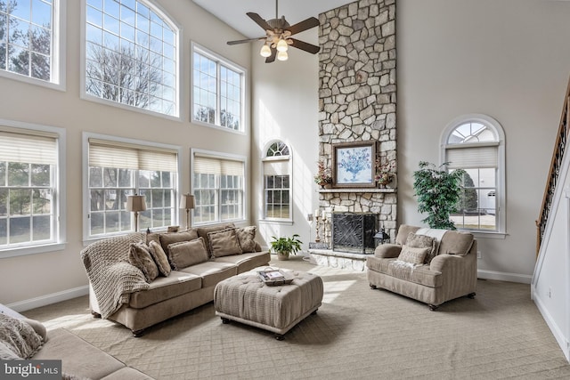 carpeted living area featuring a high ceiling, a fireplace, a ceiling fan, and baseboards