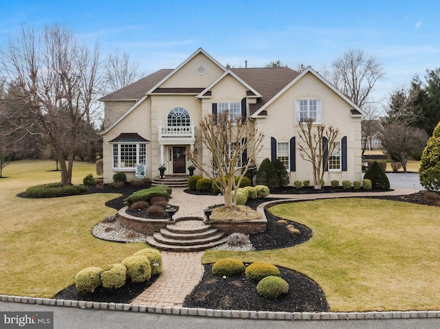 traditional-style home featuring roof with shingles, a front yard, and stucco siding