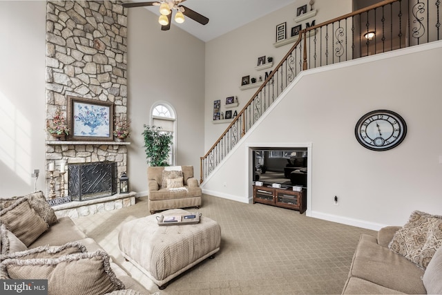 carpeted living area with ceiling fan, a fireplace, a towering ceiling, baseboards, and stairway