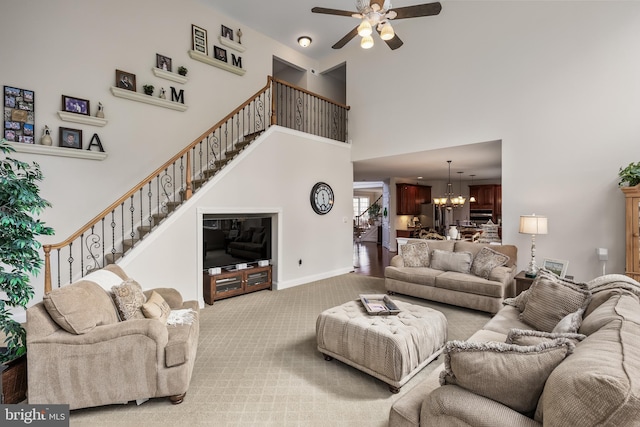 carpeted living area with baseboards, stairs, a high ceiling, and ceiling fan with notable chandelier