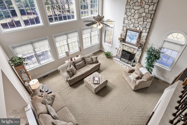 carpeted living area featuring visible vents, a healthy amount of sunlight, a stone fireplace, and a towering ceiling