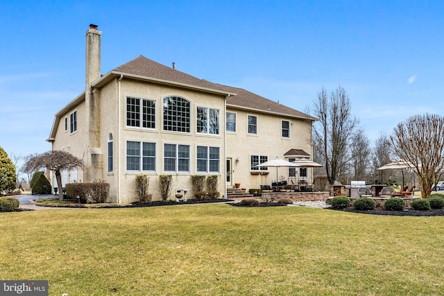 back of house with a patio, a chimney, stucco siding, a shingled roof, and a lawn